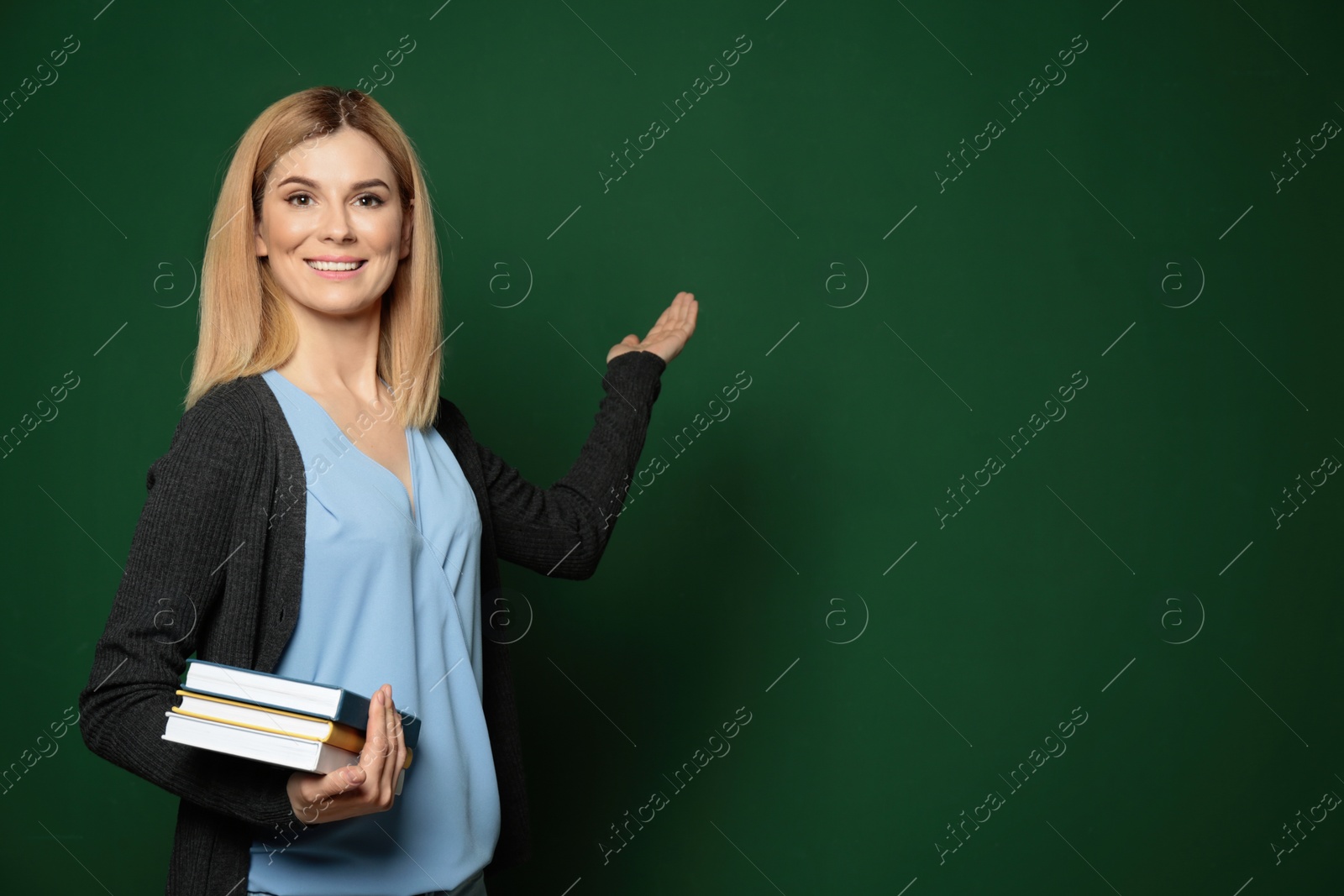 Photo of Beautiful teacher with books pointing at chalkboard, space for text
