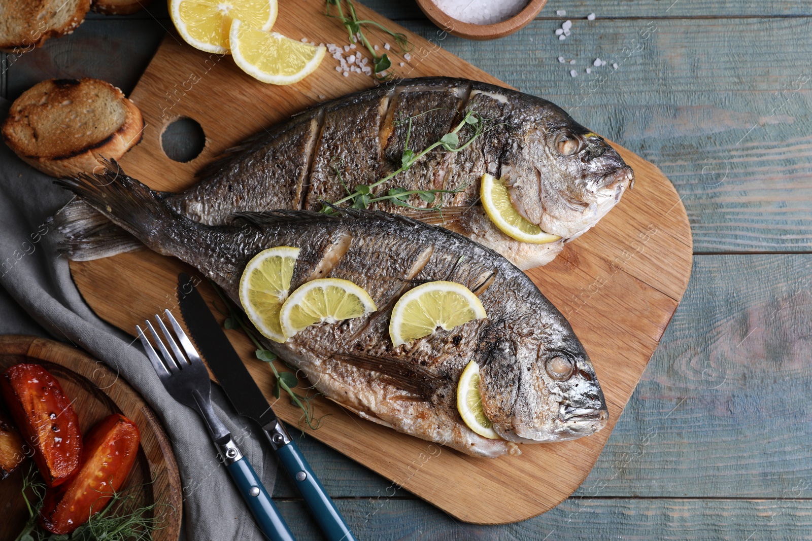 Photo of Delicious baked fish served on wooden rustic table, flat lay. Seafood