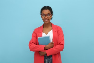 Smiling African American intern with books on light blue background