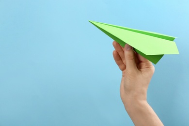 Woman holding paper plane on light blue background, closeup. Space for text