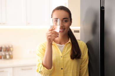 Photo of Young woman looking through glass of pure water in kitchen