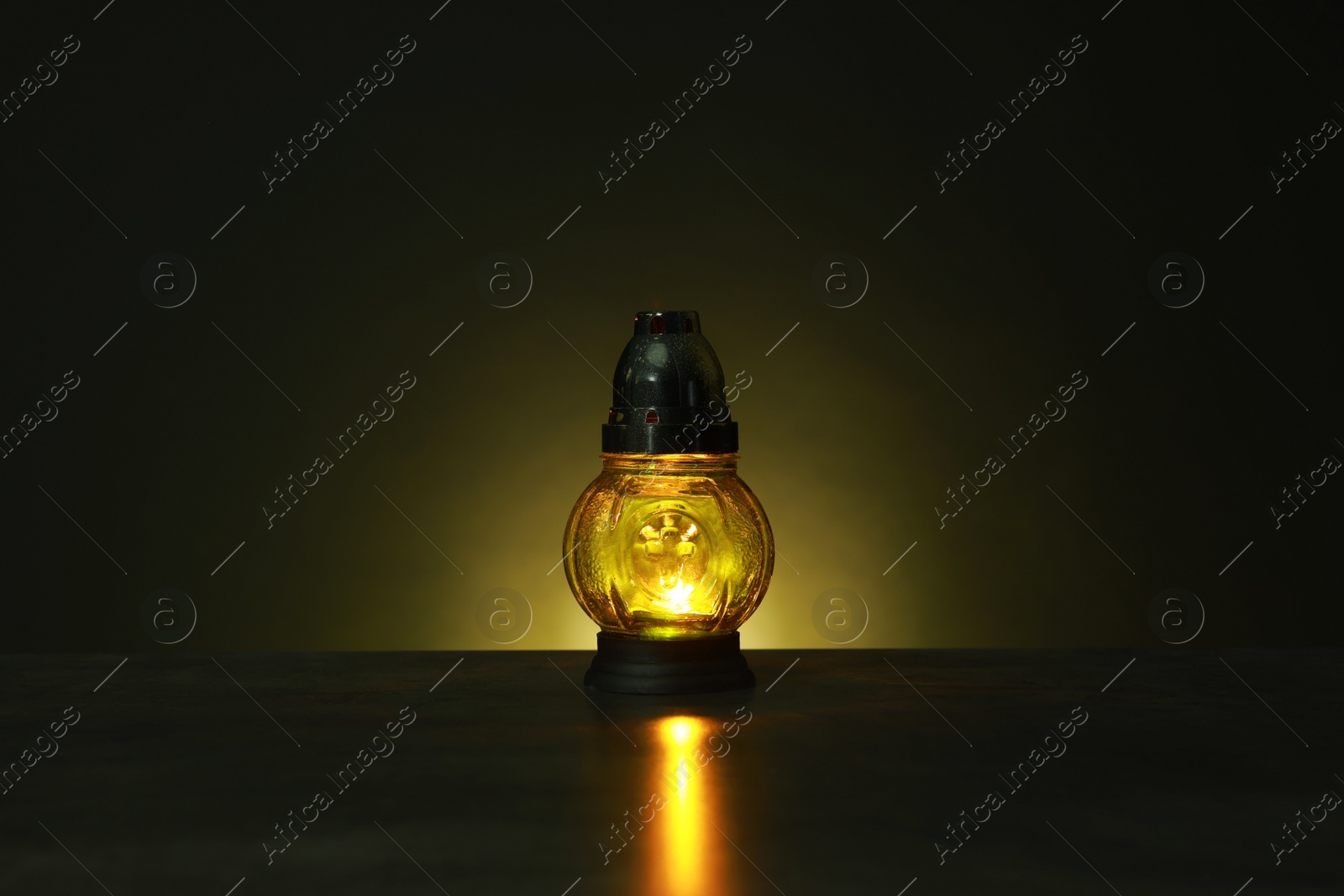 Photo of Beautiful glowing yellow grave light on table in darkness. Symbol of remembrance