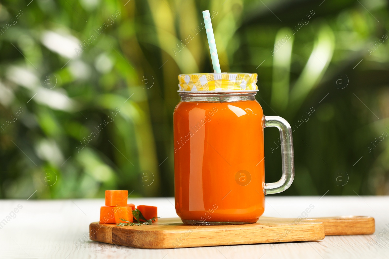 Photo of Mason jar with tasty carrot juice on white table outdoors. Space for text