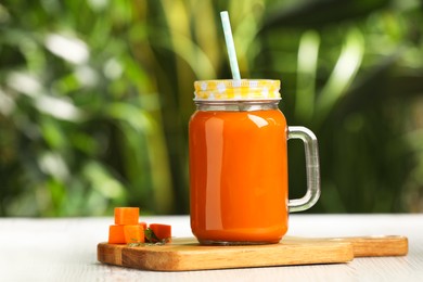 Photo of Mason jar with tasty carrot juice on white table outdoors. Space for text