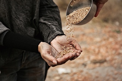 Photo of Woman giving poor homeless person bowl of wheat outdoors, closeup