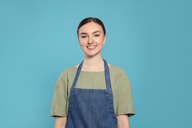 Beautiful young woman in clean denim apron on light blue background