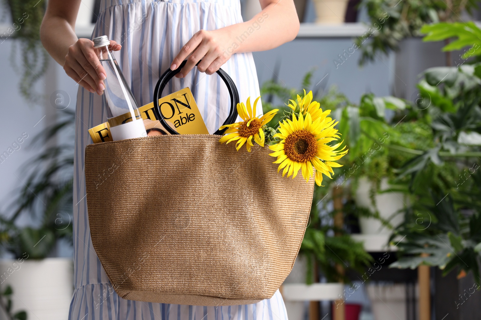 Photo of Woman putting bottle of water in beach bag indoors, closeup