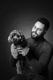 Photo of Handsome bearded man with cute dog on dark background. Black and white effect