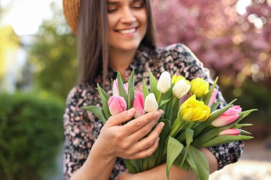 Photo of Beautiful young woman with bouquet of tulips in park, focus on hands