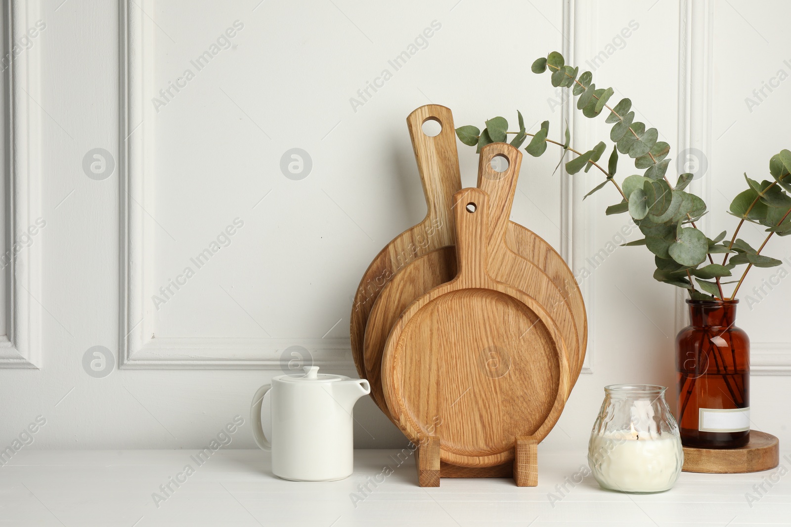 Photo of Wooden cutting boards, teapot, candle and vase with eucalyptus branches on white table, space for text