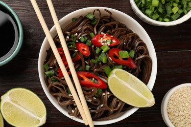 Photo of Tasty buckwheat noodles (soba) with chili pepper and sesame served on wooden table, flat lay