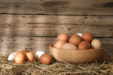 Photo of Fresh chicken eggs on dried straw near wooden wall