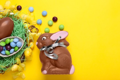 Flat lay composition with chocolate Easter bunny, eggs and candies on yellow background. Space for text