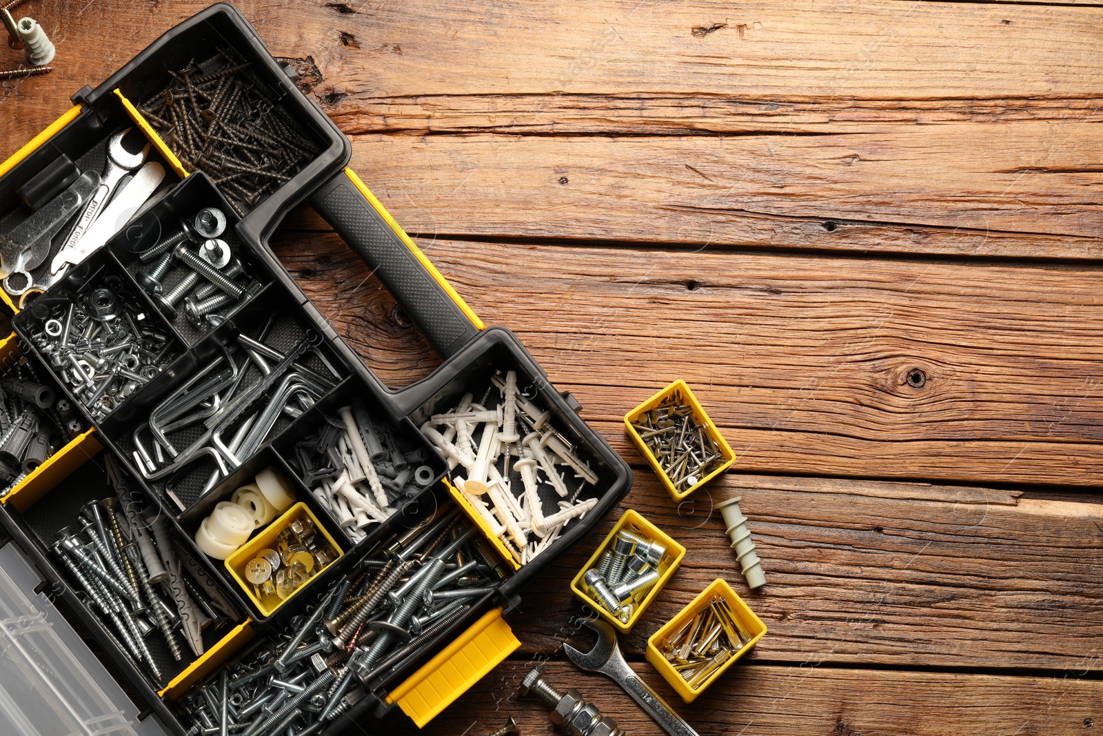 Photo of Organizer with many different fasteners and wrenches on wooden table, flat lay. Space for text