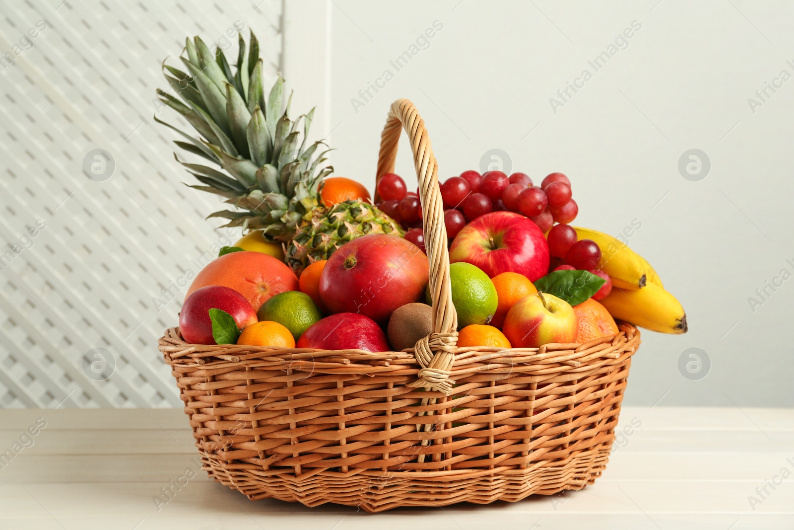 Photo of Wicker basket with different fresh fruits on white wooden table