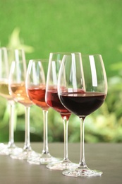 Photo of Row of glasses with different wines on grey table against blurred background