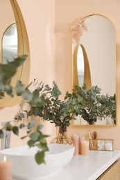 Eucalyptus branches near vessel sink on bathroom vanity. Interior design