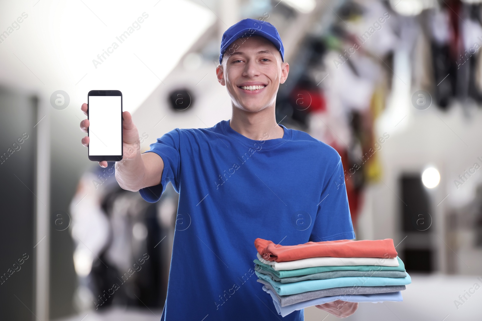 Image of Happy courier with folded clothes showing smartphone in dry-cleaning