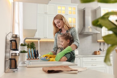 Photo of Mother and daughter in protective gloves washing plate above sink in kitchen