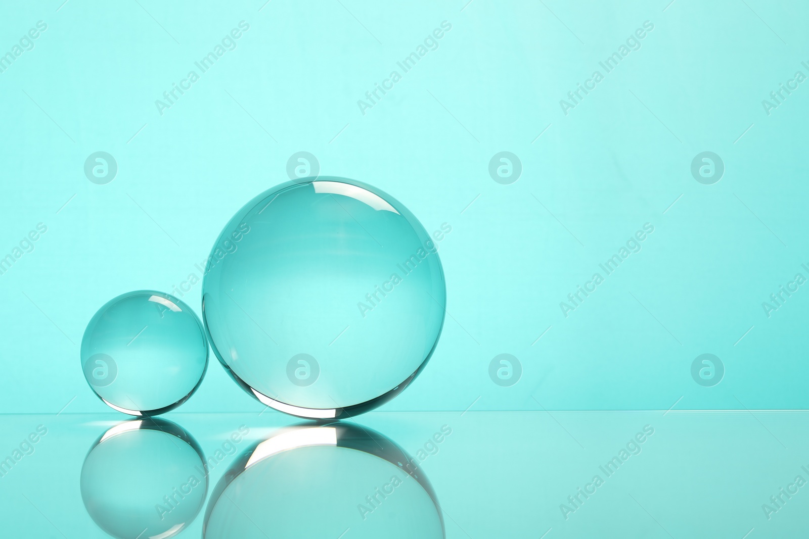 Photo of Transparent glass balls on mirror surface against turquoise background. Space for text