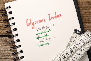 Photo of Glycemic Index. Notebook with information and measuring tape on wooden table, top view