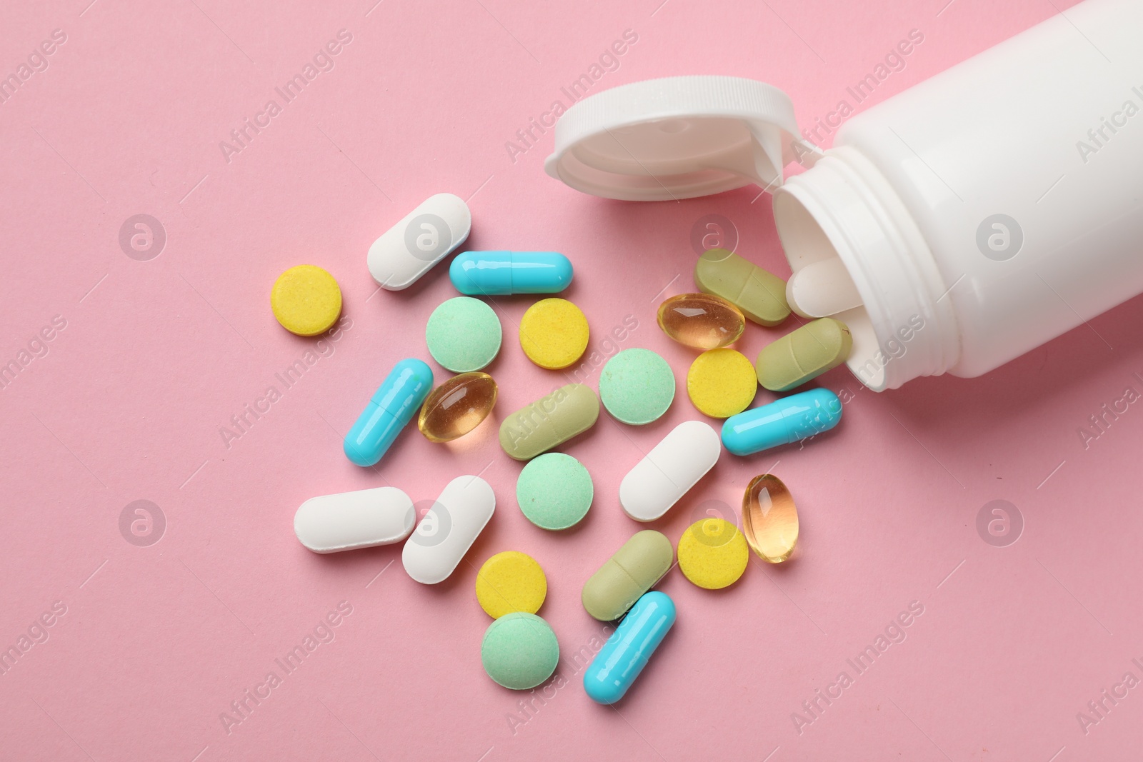 Photo of White bottle and different vitamin pills on pink background, top view