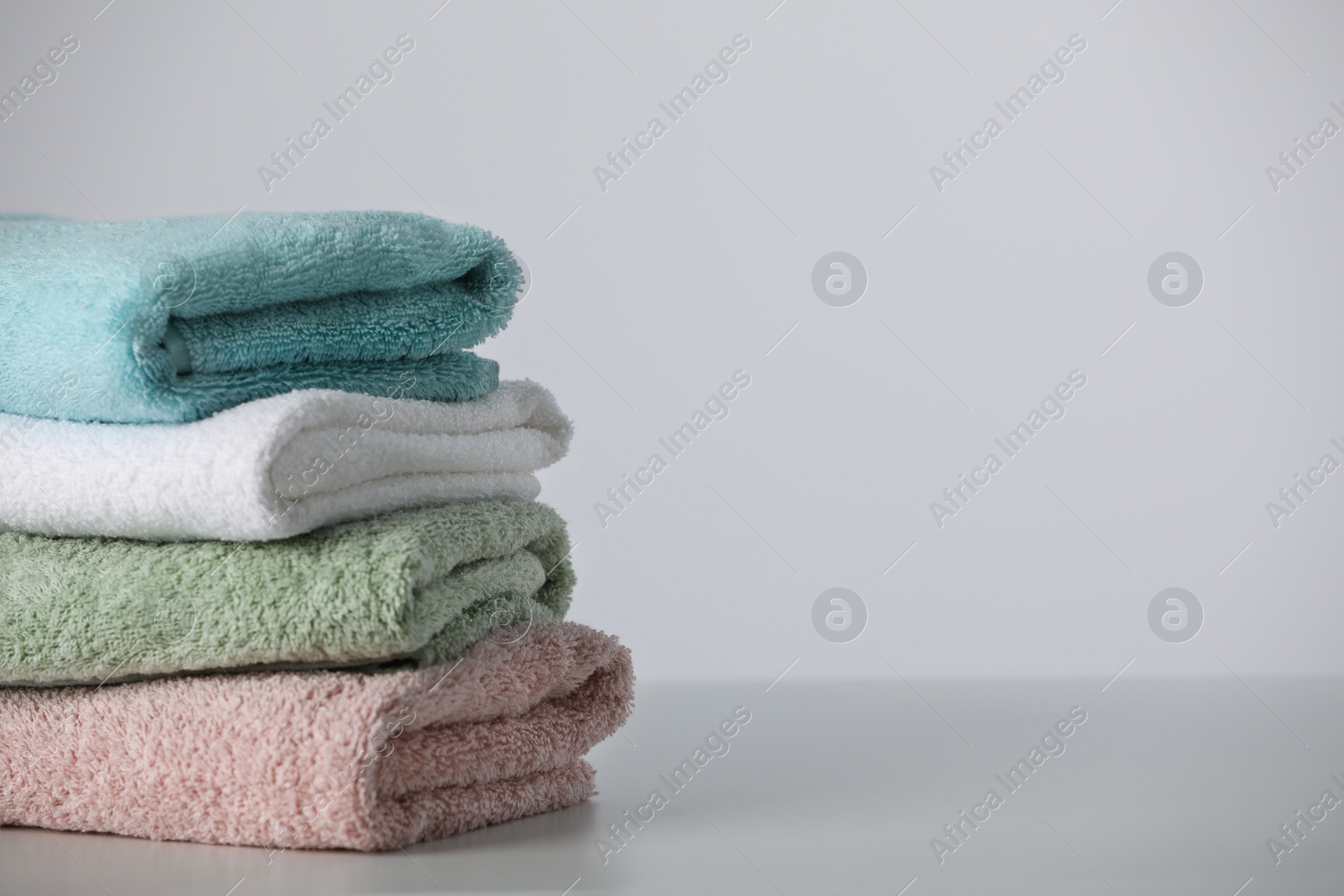 Photo of Stack of folded soft colorful towels on white table, space for text