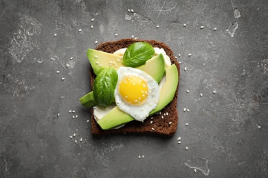 Photo of Toast bread with cream cheese, avocado and fried egg on dark background