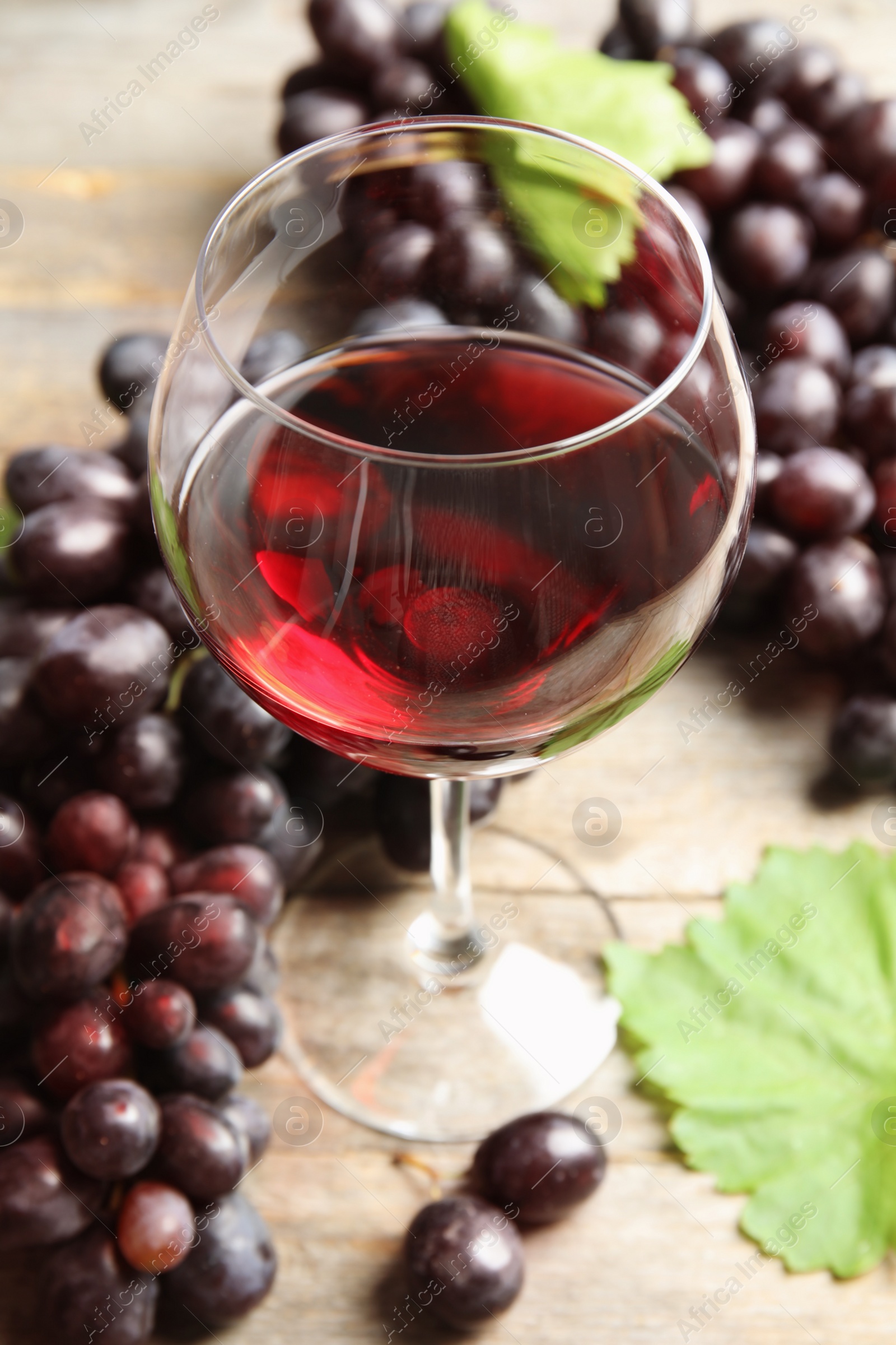 Photo of Glass of red wine and fresh ripe juicy grapes on table