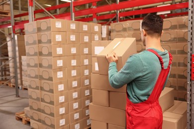 Photo of Worker stacking cardboard boxes in warehouse. Wholesaling