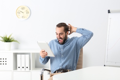 Emotional young man with tablet celebrating victory in office