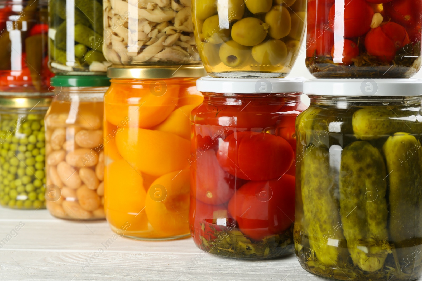 Photo of Glass jars with different pickled foods on white wooden background, closeup