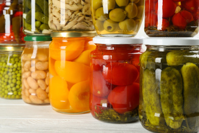 Glass jars with different pickled foods on white wooden background, closeup