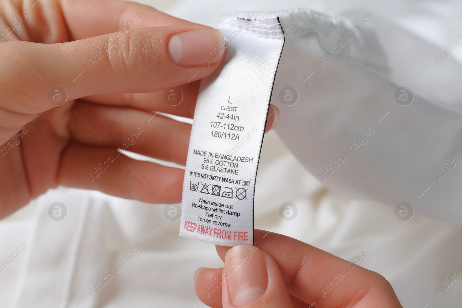 Photo of Woman reading clothing label with care symbols and material content on white shirt, closeup