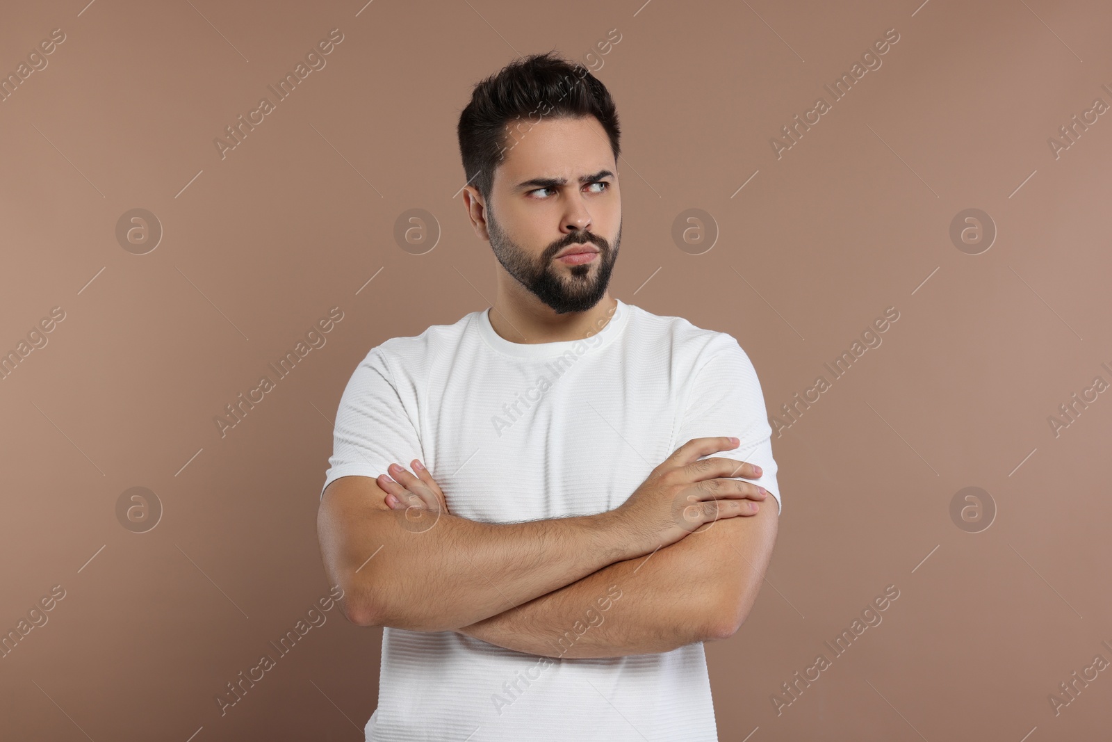 Photo of Portrait of resentful man with crossed arms on brown background