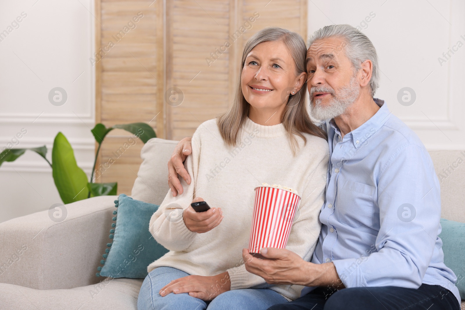 Photo of Happy senior couple with popcorn on sofa indoors