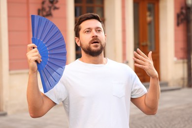 Photo of Man with hand fan suffering from heat outdoors