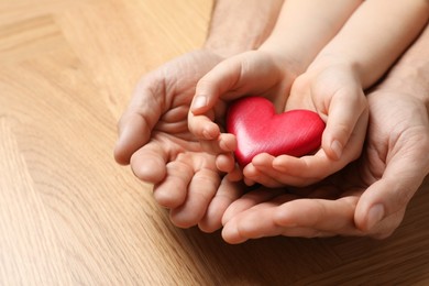 Photo of Man and kid holding red heart in hands at wooden table, closeup