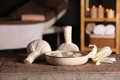 Spa composition with burning candles, lily flower and herbal bags on massage table in wellness center