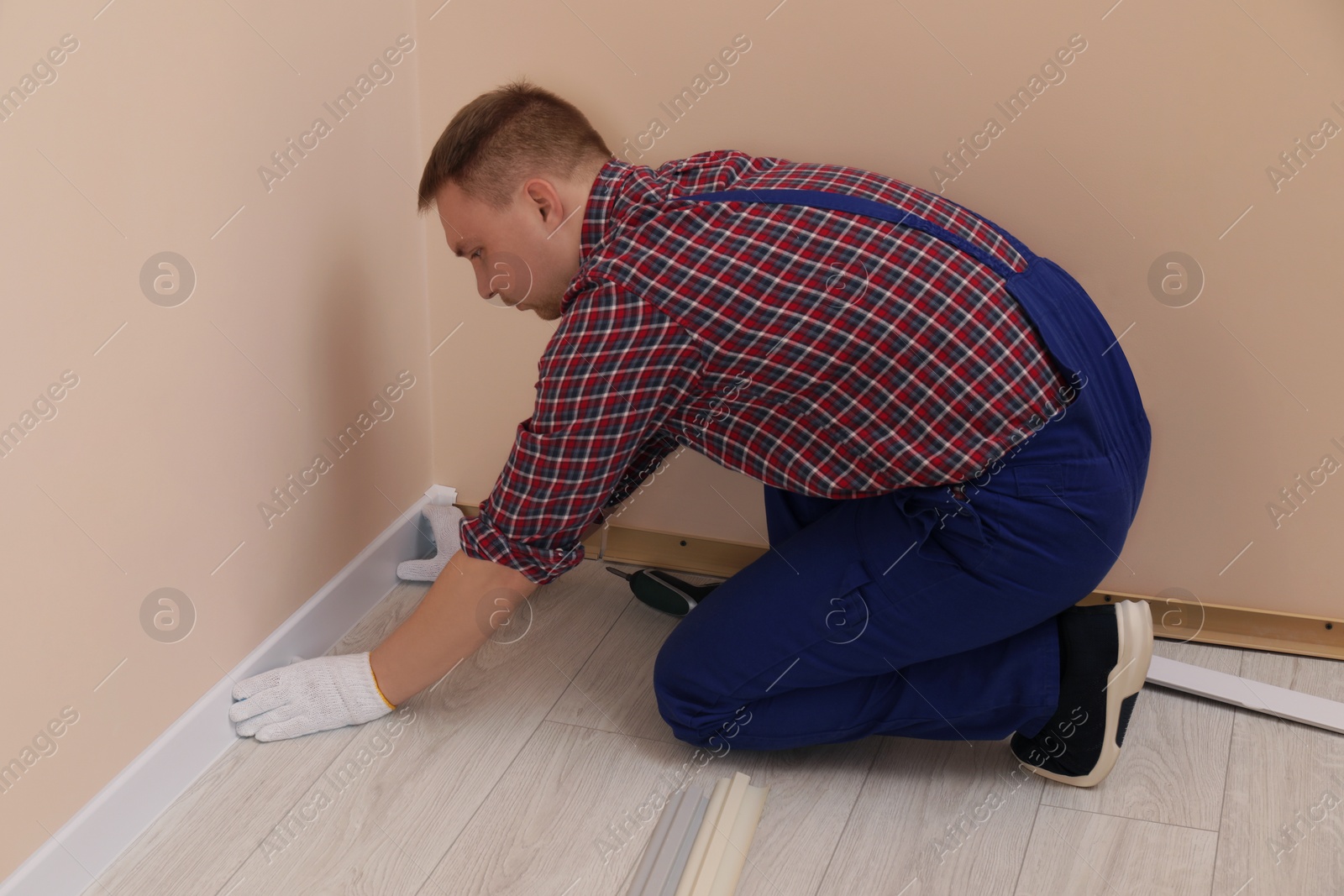 Photo of Man installing plinth on laminated floor in room