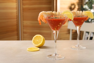 Photo of Tasty shrimp cocktail with sauce in glasses and lemon on light marble table, space for text