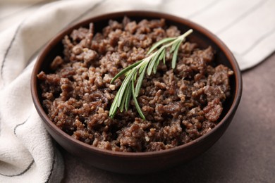 Photo of Fried ground meat in bowl and rosemary on brown textured table, closeup