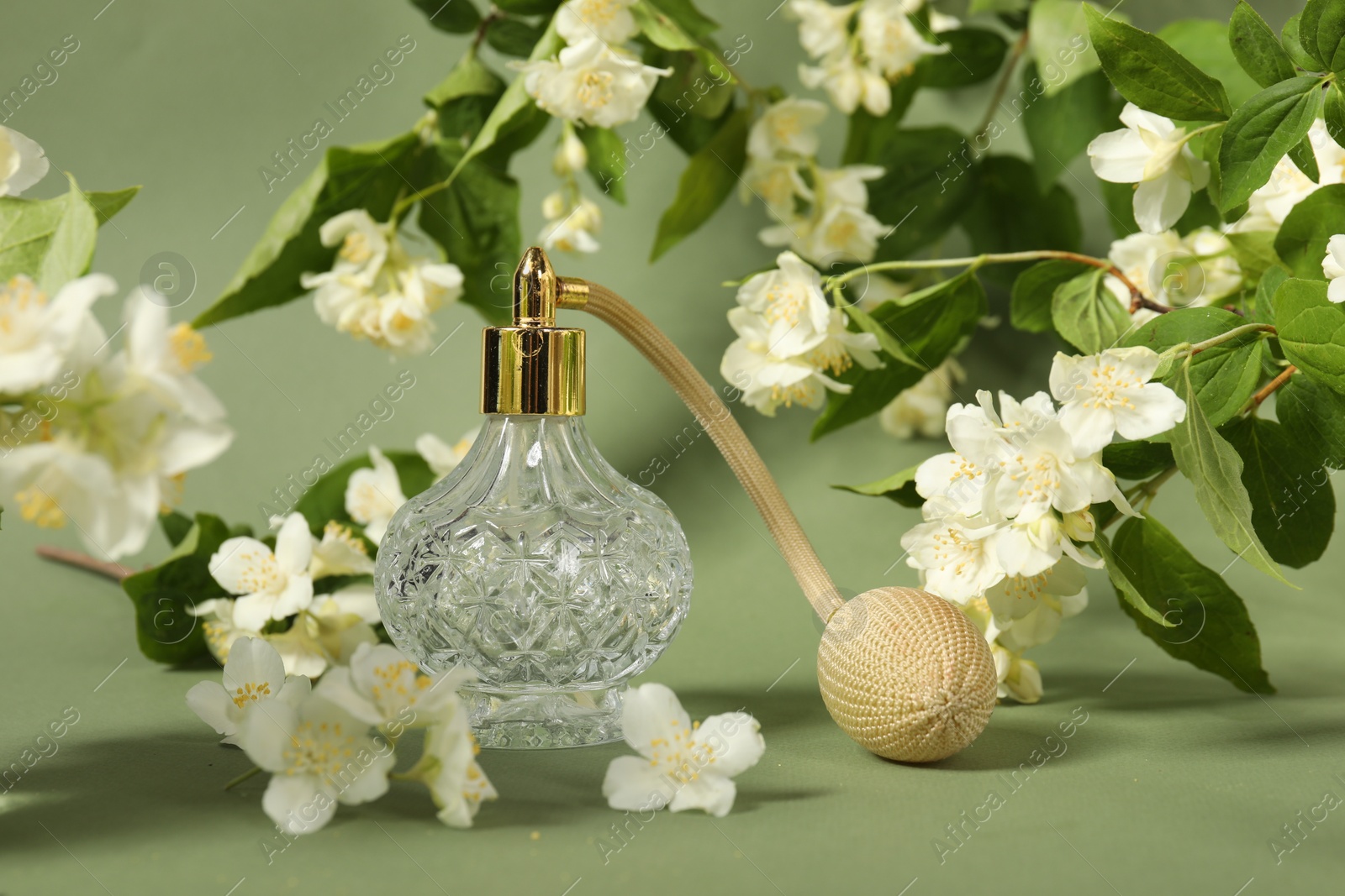 Photo of Aromatic perfume in bottle among beautiful jasmine flowers on pale green background