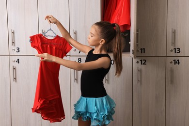 Photo of Little girl holding hanger with beautiful dress in locker room