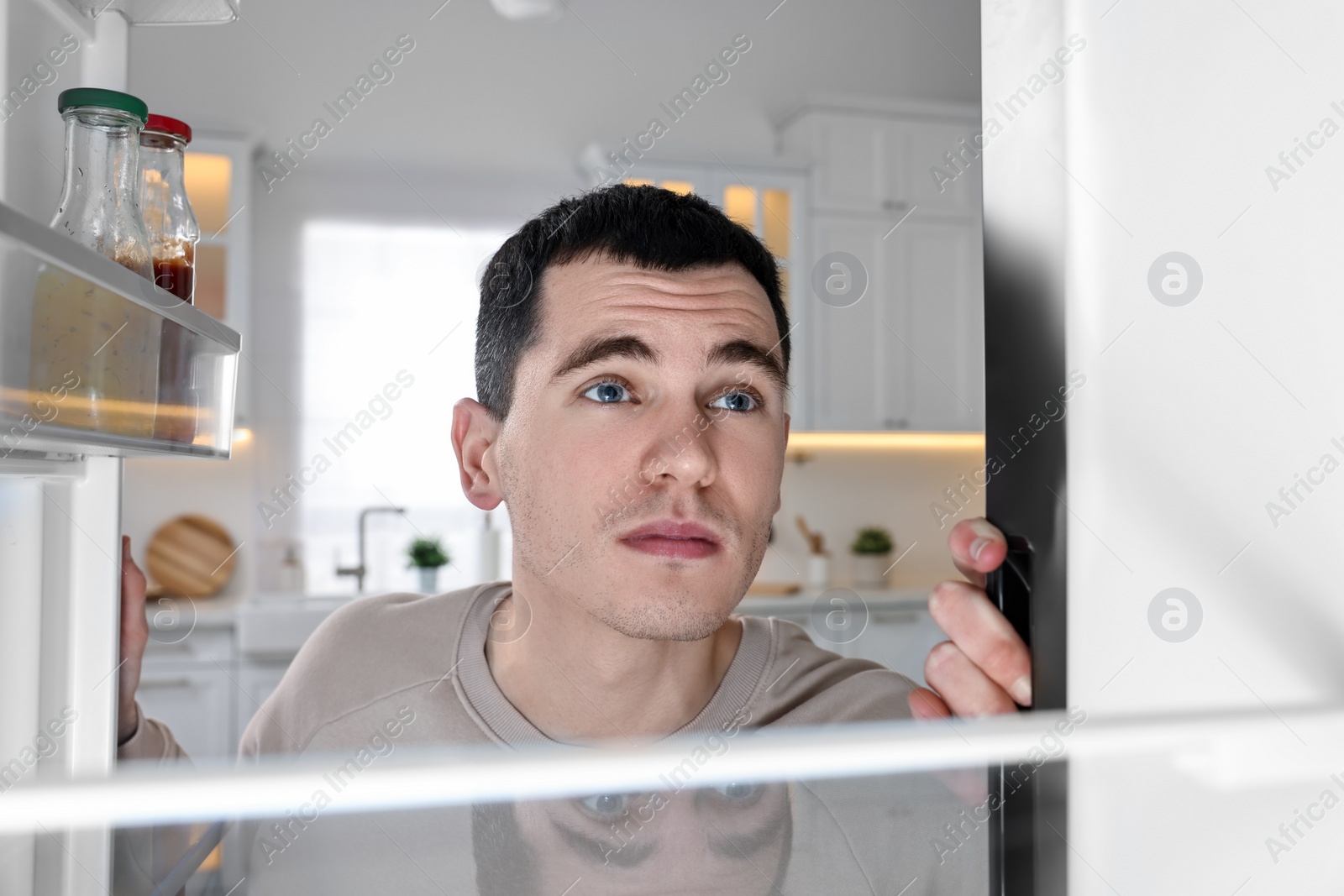 Photo of Upset man near empty refrigerator in kitchen, view from inside