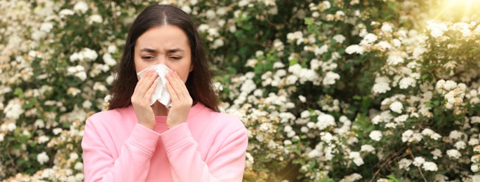 Woman suffering from seasonal pollen allergy near blossoming tree on spring day. Banner design with space for text