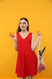 Photo of Woman with string bag of fresh vegetables on orange background