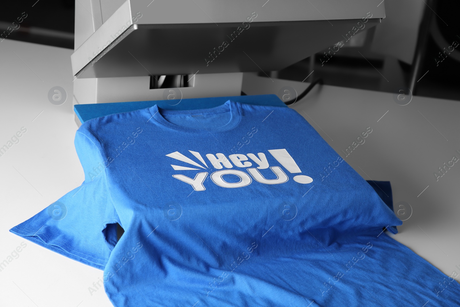 Photo of Printing logo. Heat press with blue t-shirt on white table