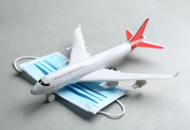 Photo of Toy airplane and medical mask on grey stone background, closeup. Travelling during coronavirus pandemic