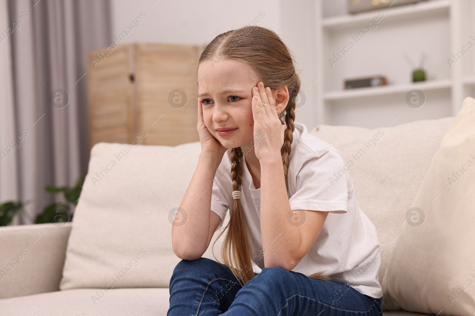 Photo of Little girl suffering from headache on sofa indoors